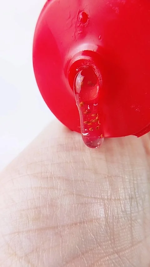 Point of view pouring clear gel liquid with raspberry extract onto hand ski.. Stockbeeldmateriaal 346584567