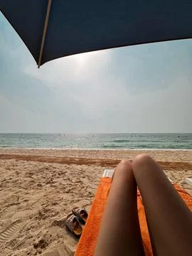 Point-of-view shot of legs under a beach umbrella looking at the sea. Stock Photos