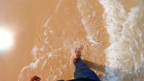 Point of view shot of a man walking on the beach with sea waves touching the leg Stock Footage