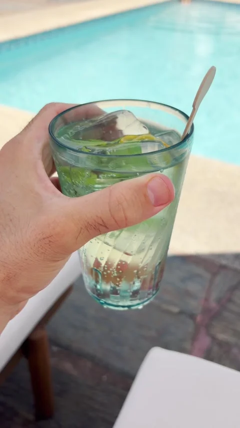 Point of view vertical video hand holding cold fresh cocktail by swimming pool 動画素材 339199442