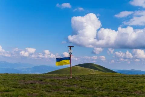 A pointer with a Ukrainian flag set at the peak of a big green mountain Foto stock
