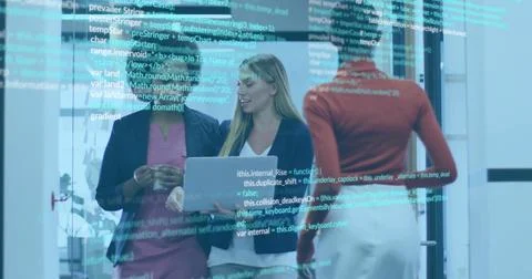 Pointing three women discussing code on glass partition in office, holding Foto stock