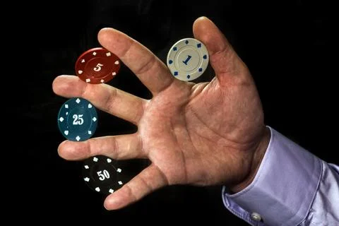 Poker chips of different colors between the fingers of a man's hand Photos