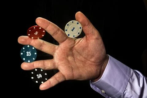 Poker chips of different colors between fingers of male hand on black background Photos