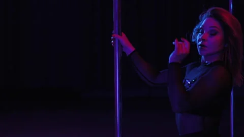 A pole dancer, dressed in a black outfit adorned with decorative studs and Stock Footage 284848648