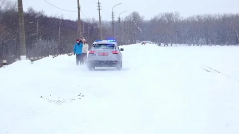 Police car drives in snow while people walk along snowy road in winter Stock Footage 328138919