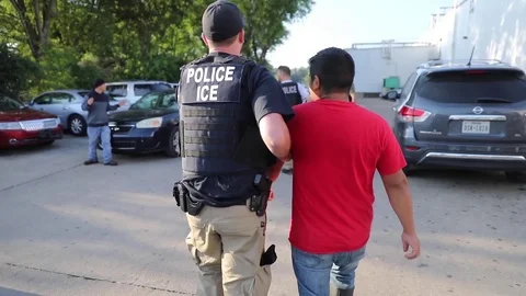 Police ICE escorting suspected illegal worker through carpark towards vehicle Stock Footage 113796487