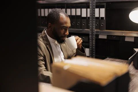 Policeman drinking coffee and analyzing clues using laptop Stock Photos