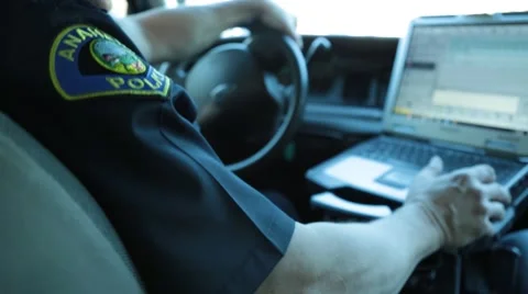 Policeman sitting in the driver's seat of his patrol car looking at a laptop Video stock 59165472