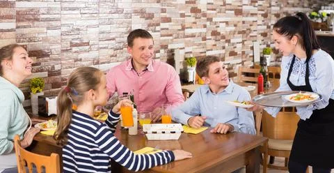 Polite attractive waitress bringing ordered dishes to family Stock-Fotos