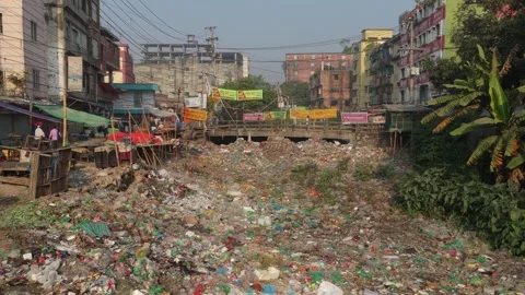 Polluted river full of plastic trash flowing under bridge in Dhaka Stock Footage 325364544