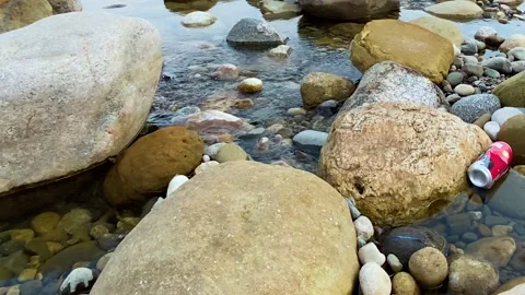 Pollution: Red discarded soda can floating on rocky water. 스톡 동영상 333926926