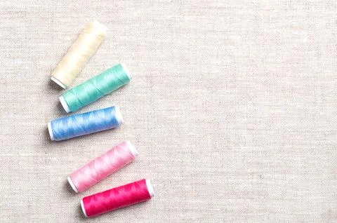 Polyester sewing thread spools randomly distributed on linen fabric Stock Photos