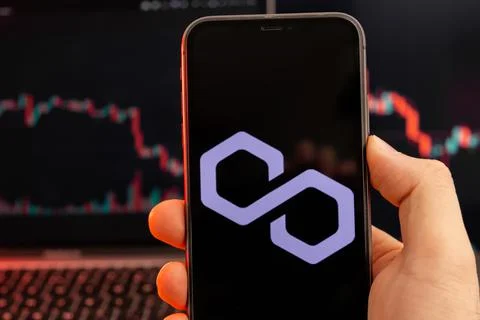 Polygon MATIC cryptocurrency logo on the screen of smartphone in mans hand with Stock Photos