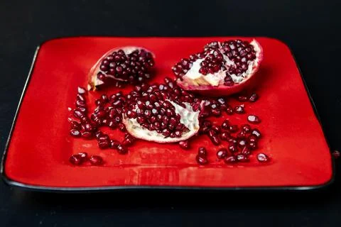 Pomegranate arils macro closeup on red plate. Fresh pomegranate seeds texture Stock Photos