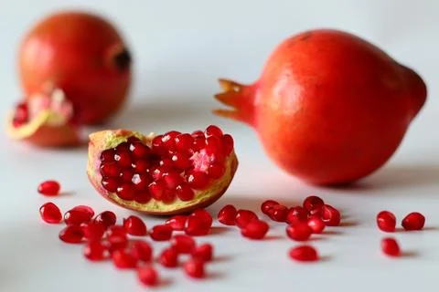 Pomegranate. Open fruit with glistening ruby red arils on a white surface, ca Stock Photos