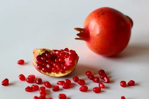 Pomegranate. Open fruit with glistening ruby red arils on a white surface, ca Stockfoto's