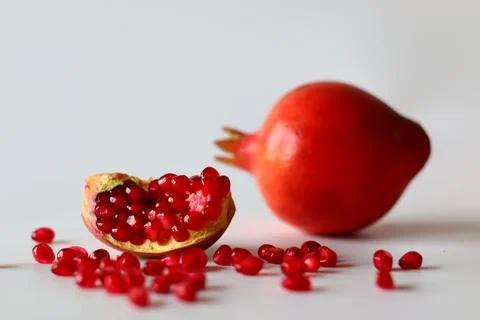 Pomegranate. Open fruit with glistening ruby red arils on a white surface, ca Stock Photos