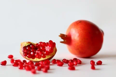 Pomegranate. Open fruit with glistening ruby red arils on a white surface, ca Stock Photos