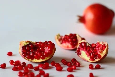 Pomegranate. Open fruit with glistening ruby red arils on a white surface, ca Stockfoto's