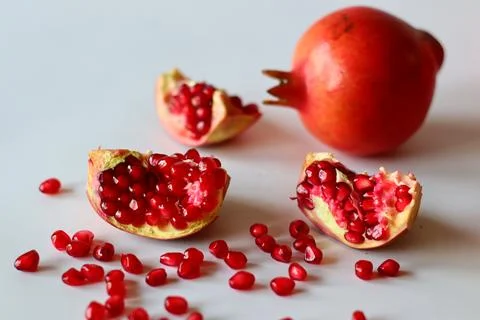 Pomegranate. Open fruit with glistening ruby red arils on a white surface, ca Stock Photos