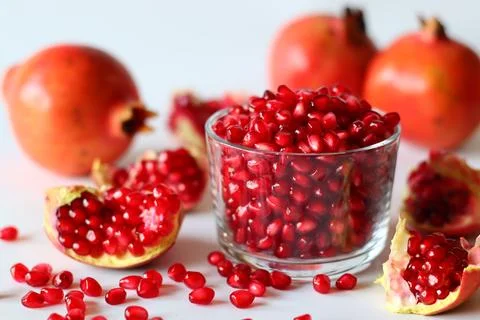Pomegranate. Open fruit with glistening ruby red arils on a white surface 스톡 사진