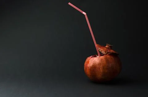 Pomegranate with a straw for drinks on a black background. Natural juice Stock Photos