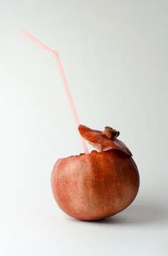 Pomegranate with a straw for drinks on a light background. Natural juice Stock Photos