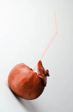 Pomegranate with a straw for drinks on a light background. Natural juice Stock Photos