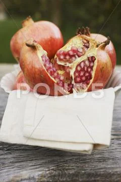 Pomegranates, whole and halved, on cloth in white bowl Stock Photos