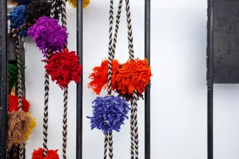 Pompons on a colored thread on a white wall and metal lattice. Stock Photos