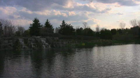 A pond and small waterfall at sunset with backlit clouds Stock Footage 398715