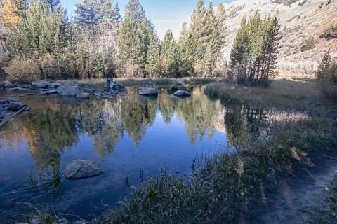 Pond with bright reflections on path to mountains in early dawn Stock Photos