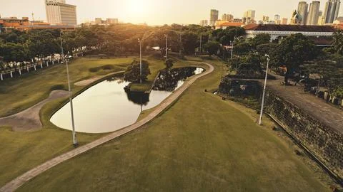 Pond with sun reflection at designed green park aerial. Green grass valey with Stock Photos