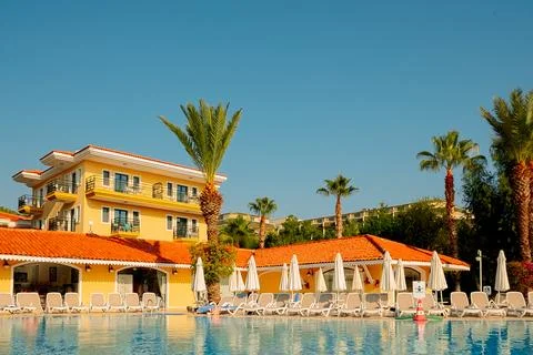 Pool area is seen with clear blue water reflecting sunlight. Chairs placed al Stock Photos