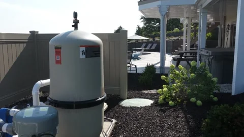 Pool heat pump and filter tank sit within mulched garden bed beside daylilies Stock Footage 342576996