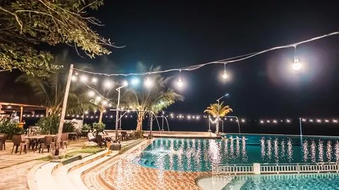 A pool with lights hanging above it and a beach setting Stock Photos