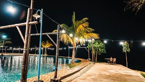 A pool with lights on the trees and a table with chairs Stock Photos