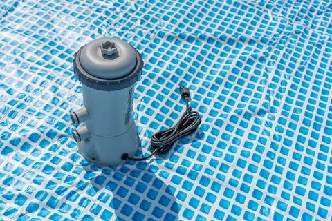 The pool pump is standing on the blue surface, the cable is wound up. Stock Photos