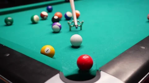 Pool table close-up as a cue aims at the red 3 and it drops into a pocket, with Stock Footage 327887241