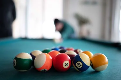 Pool table with shiny balls, in the background player ready to shoot. Stock Photos