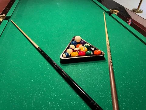 A pool table shows balls in a triangle shape while two cues sit ready for u.. Фото