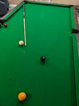 A pool table with some balls and a cue stick on the table Stock Photos