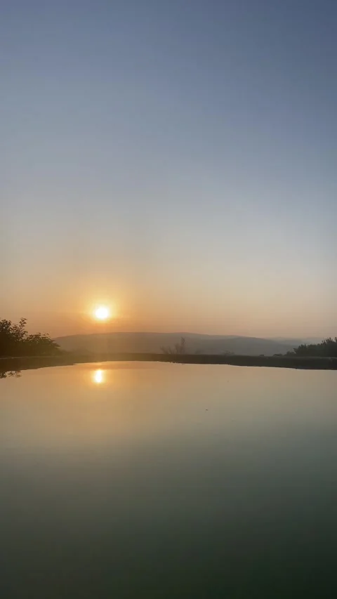 Pool water reflecting sunset with distant hill and bright summer sky 🌞🌊 動画素材 310965171