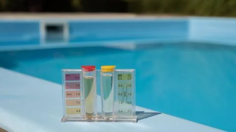 A pool water testing kit with pH and chlorine levels is placed on the pool's Stock Photos