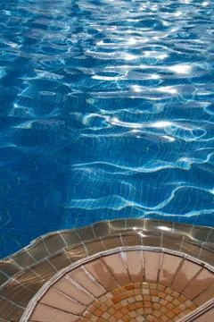 Poolside with steps and clean blue water under summer sun Stock Photos