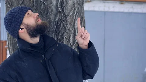 Poor bearded man on a winter day wearing headphones showing his index finger up Stock Footage 87642496