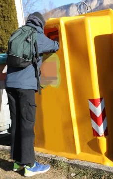 Poor boy with a backpack searching in the yellow rubbish bin for something to Foto stock