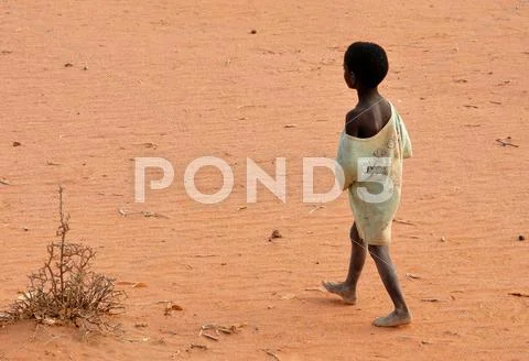 Photograph: Poor boy walking barefoot on the sandl. Poverty concept ...