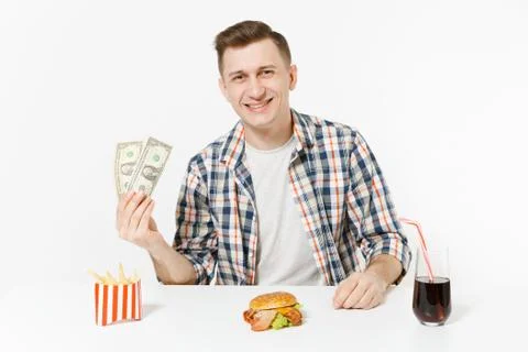Poor fun man sitting at table with two dollar bills, burger, french fries, co Stock Photos